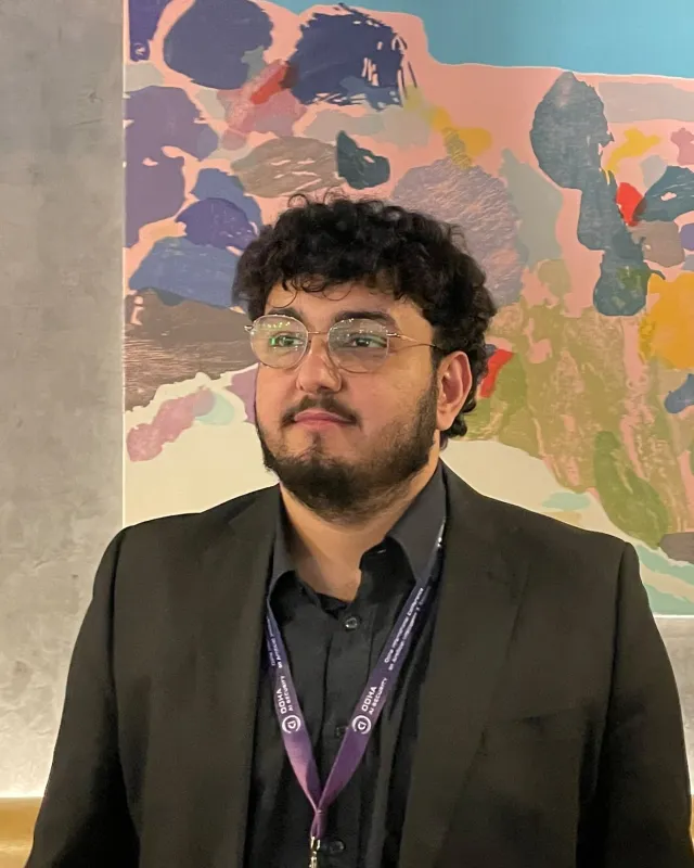 Fayez Al Khasawneh in a dark blazer, looking to the side, in front of a colourful mural
