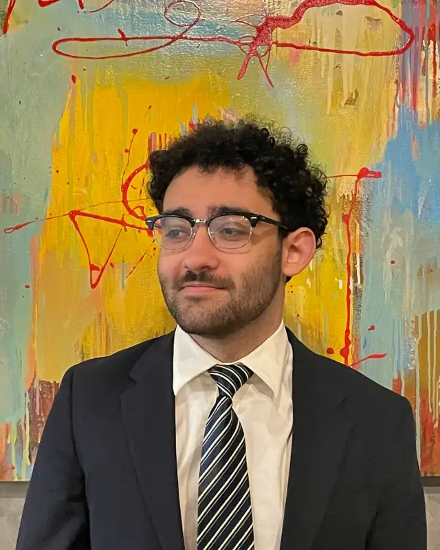 Mahmoud Al Azzeh in a suit and striped tie, in front of an abstract painting